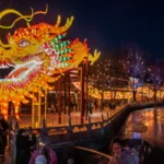 Ano-Novo Chinês, lanterna de dragão gigante e iluminada, com pessoas caminhando em uma orla à noite.