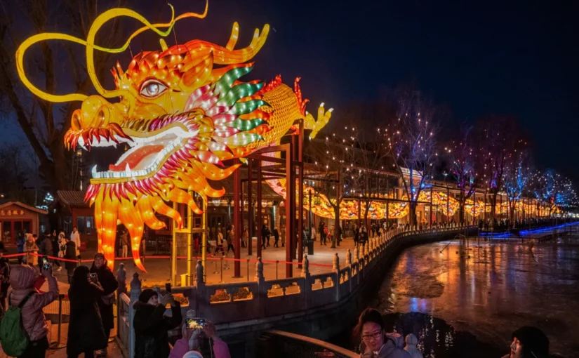 Ano-Novo Chinês, lanterna de dragão gigante e iluminada, com pessoas caminhando em uma orla à noite.