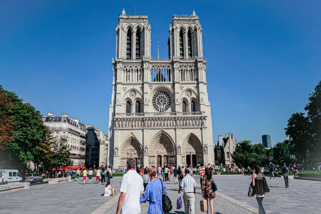 Vista frontal da Catedral de Notre-Dame em Paris, com pessoas caminhando na praça em frente.