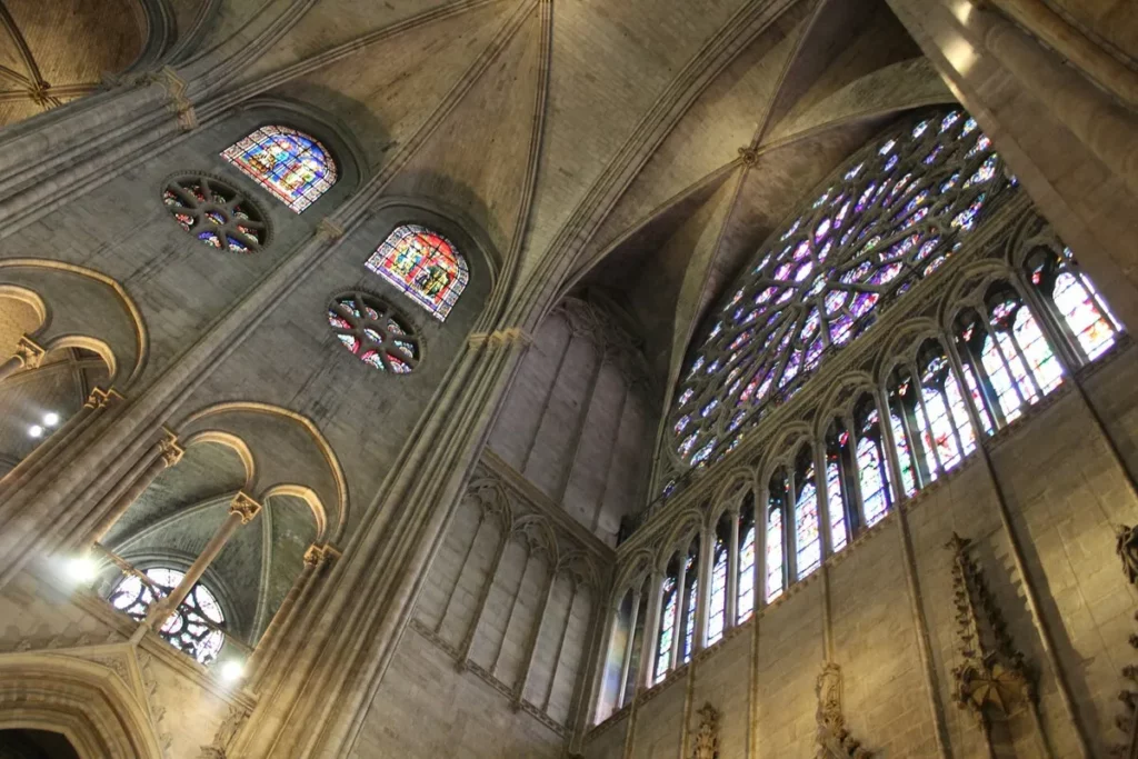 Vista do interior da Catedral de Notre-Dame em Paris, mostrando o teto abobadado de pedra e os impressionantes vitrais góticos.