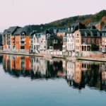 Uma fila de casas coloridas à beira de um rio calmo, com suas fachadas refletidas na água, em uma cidade pitoresca na Europa.