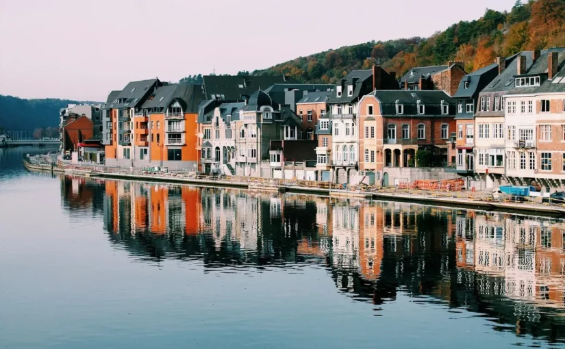 Uma fila de casas coloridas à beira de um rio calmo, com suas fachadas refletidas na água, em uma cidade pitoresca na Europa.
