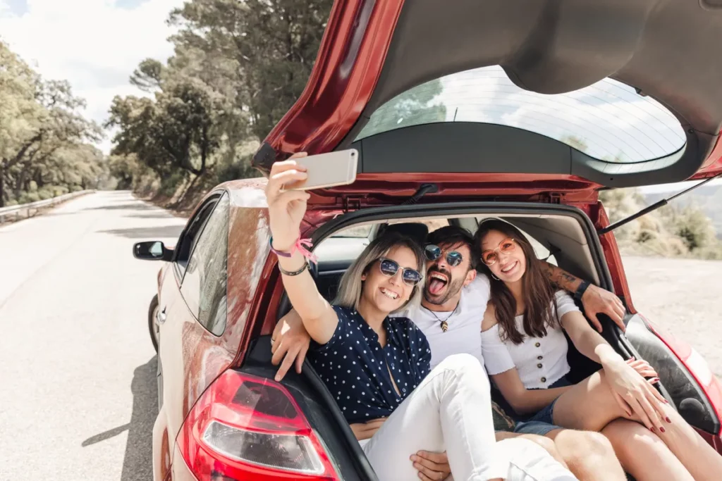 Três amigos tirando uma selfie no porta-malas de um carro, representando a alegria de um passeio de "bate-volta".
