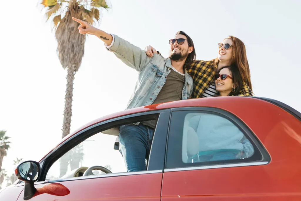  Três amigos em um carro conversível, um homem apontando para o horizonte, simbolizando a aventura de um "bate-volta".