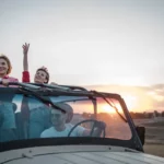 Três amigos em um jipe, comemorando e se divertindo durante um passeio de "bate-volta" ao pôr do sol.