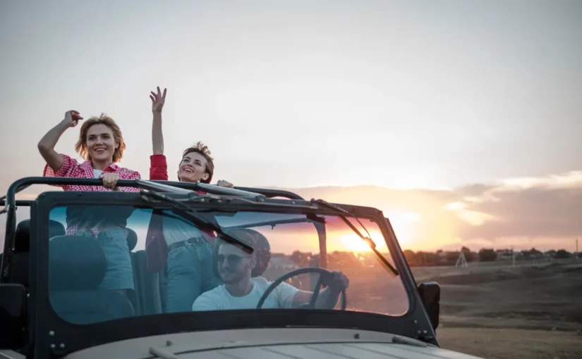 Três amigos em um jipe, comemorando e se divertindo durante um passeio de "bate-volta" ao pôr do sol.