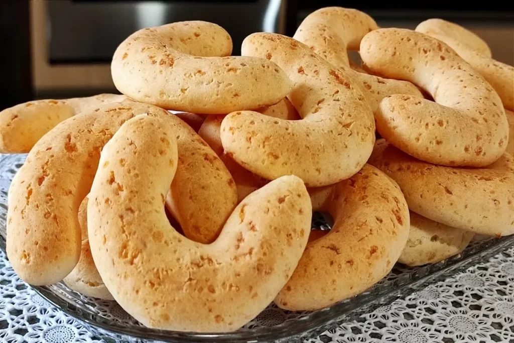 Uma bandeja de vidro cheia de chipas douradas em forma de ferradura, dispostas em uma pilha, com uma toalha de renda branca por baixo.
