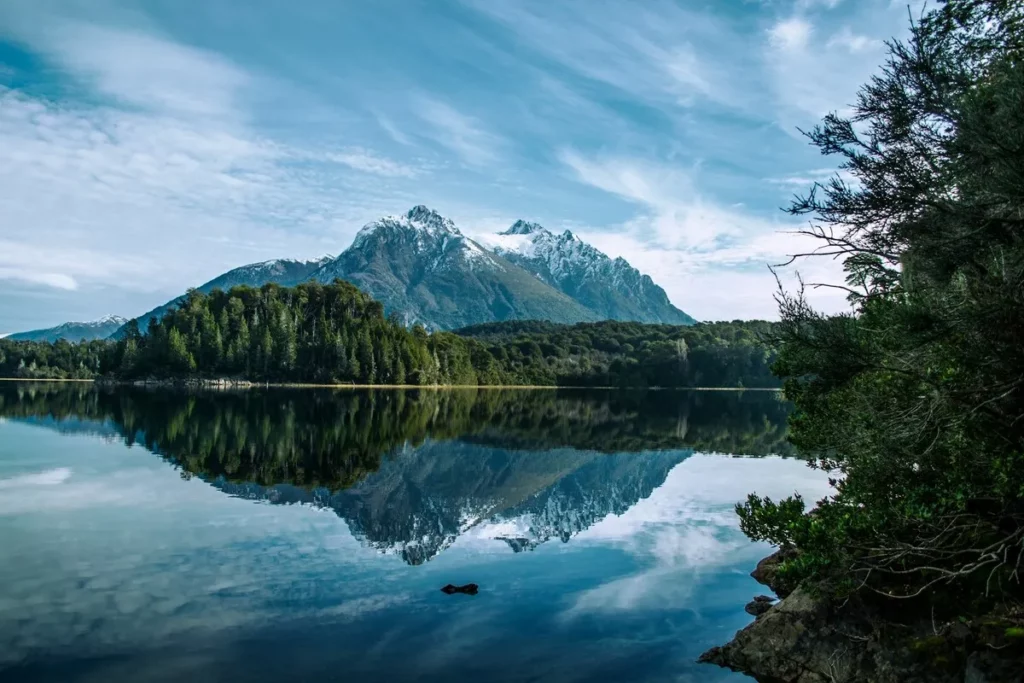 Lago e montanhas nevadas em Bariloche, com reflexo perfeito na água, representando as "coisas legais para fazer em Bariloche" para amantes da natureza.