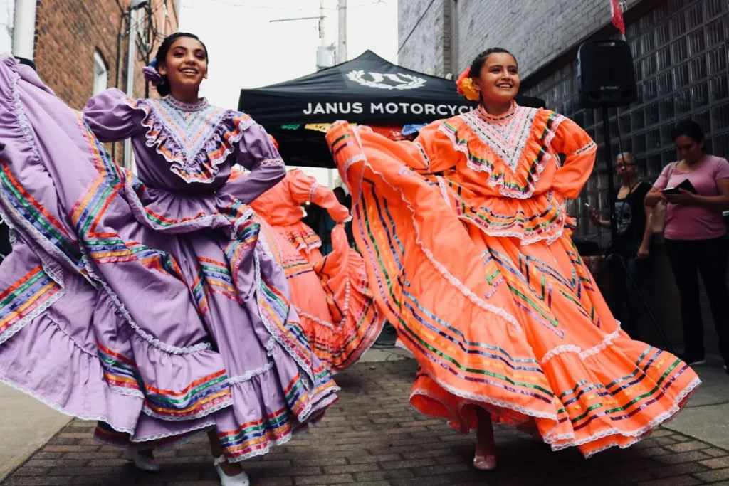 Duas meninas dançando em um festival de rua, usando vestidos folclóricos coloridos e rodados, representando a cultura e tradição.