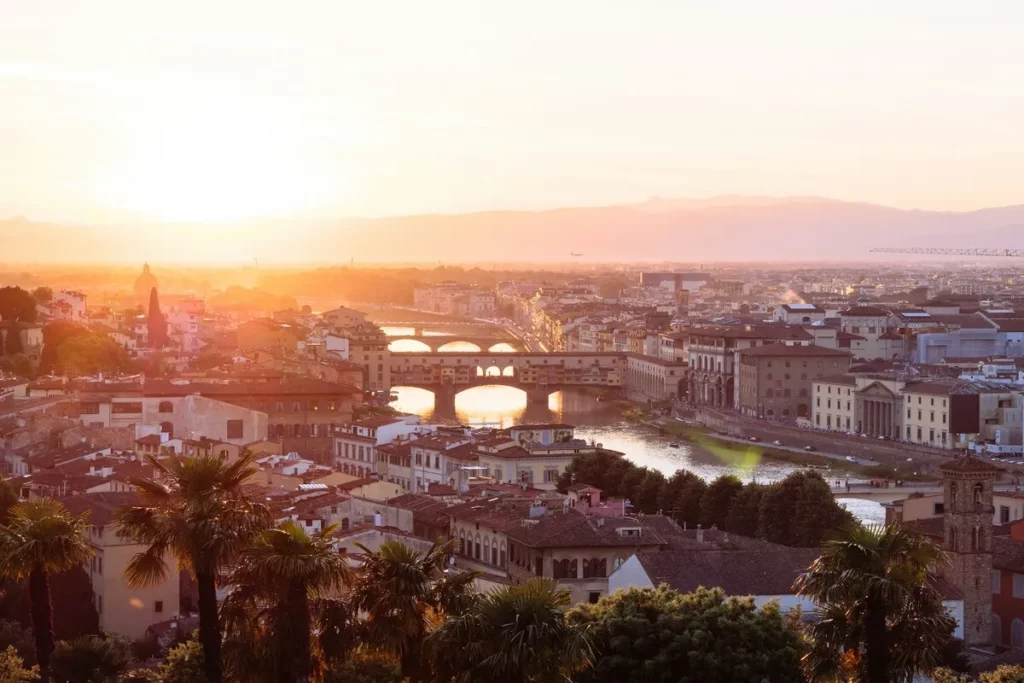 Dicas de viagem para a cidade de Florença, na Itália, com vista do Rio Arno e da Ponte Vecchio ao pôr do sol.