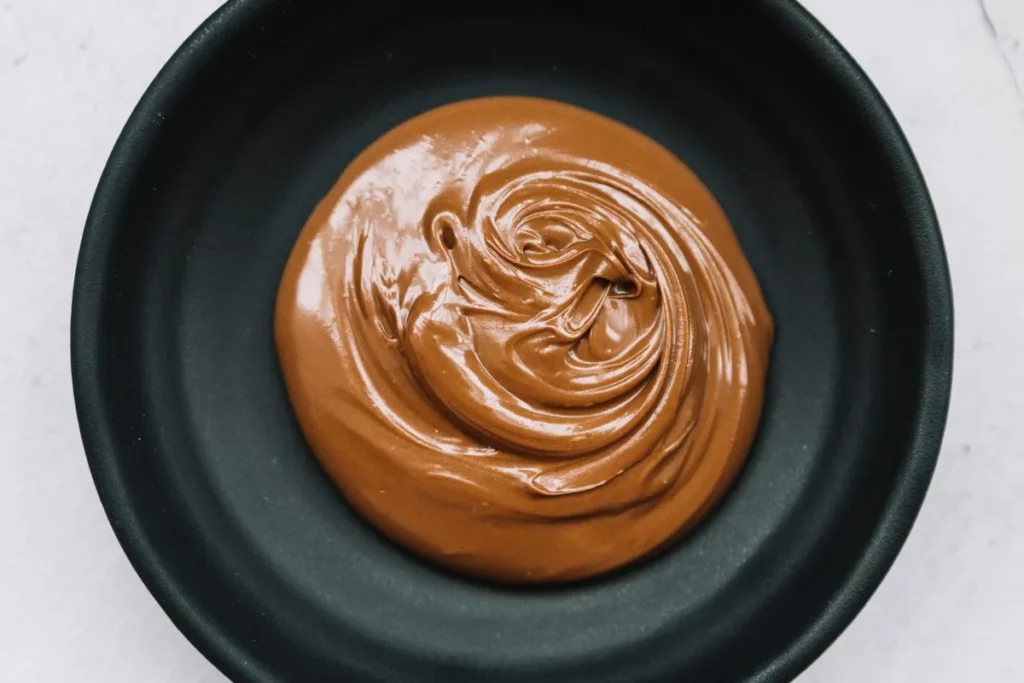 Doce de leite cremoso e brilhante em um prato preto, com sua textura e cor em destaque.