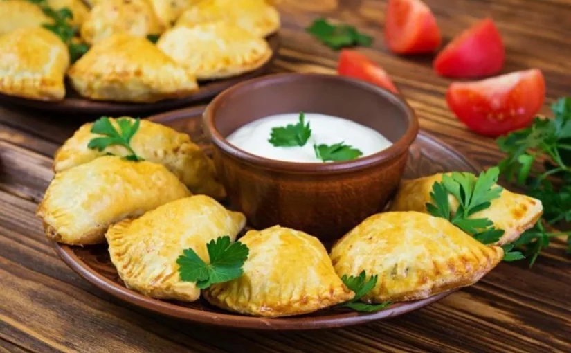 Empanada argentina assada servida em prato de cerâmica com molho.
