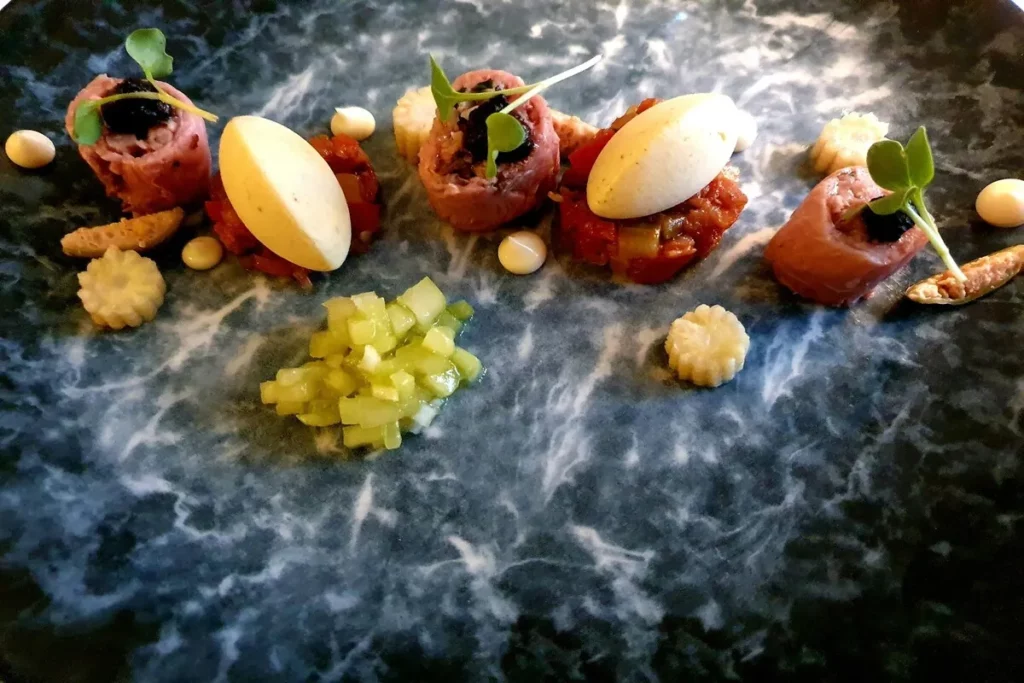 Prato gourmet de alta gastronomia com carne, molho e espuma em um prato de mármore escuro.