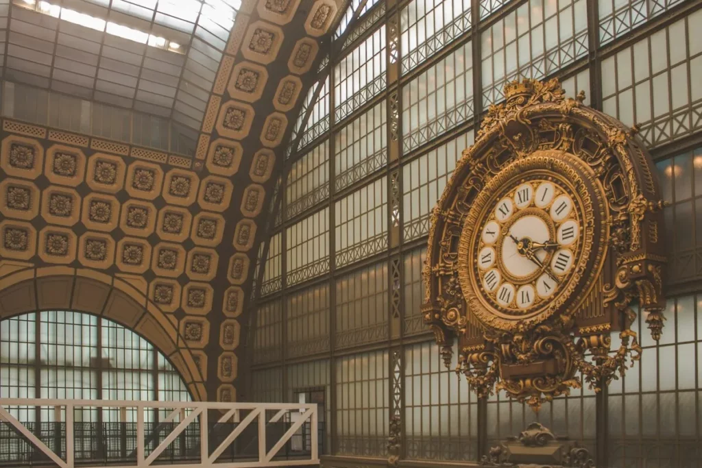 O majestoso relógio dourado no interior do Musée d'Orsay, um dos museus de Paris mais famosos, com a sua arquitetura de estação de comboios e o teto de vidro. A imagem capta a beleza única do edifício.