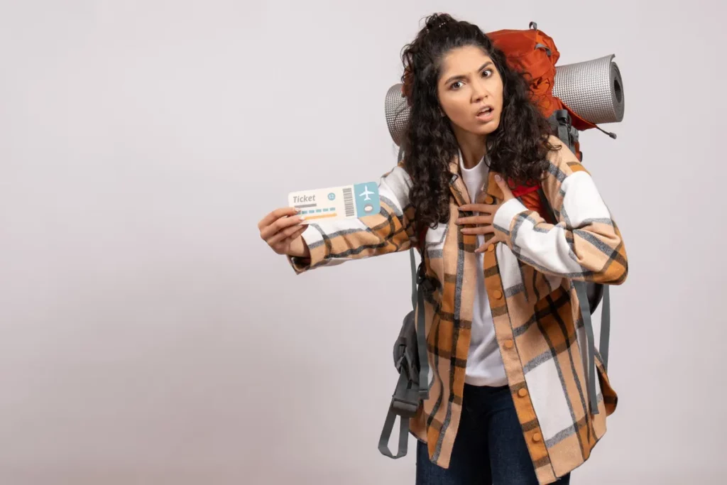 Mulher com mochila de viagem e expressão de choque, segurando uma passagem de avião, ilustrando perrengues comuns em viagens.