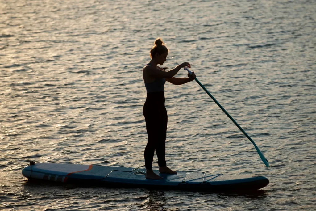 Silhueta de uma mulher praticando stand up paddle em um lago ou mar calmo.