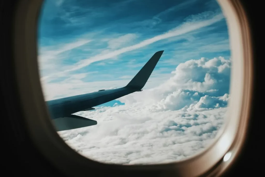 Viagem barata internacional: Vista da asa de avião com nuvens e céu azul claro.