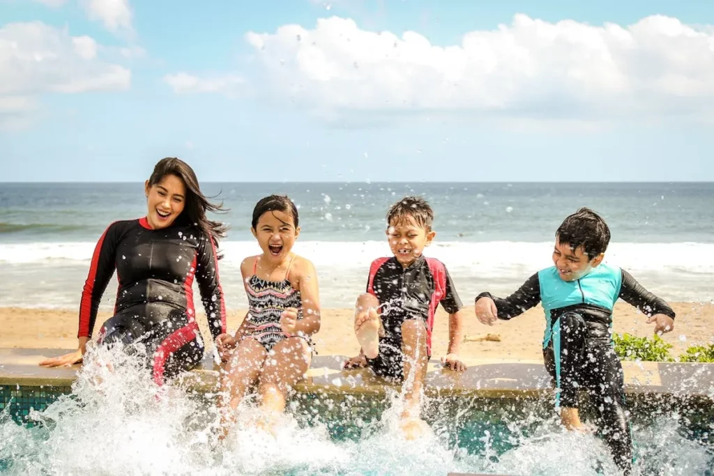 Uma família de quatro pessoas na beira de uma piscina com vista para o oceano, rindo e se divertindo com os respingos de água.