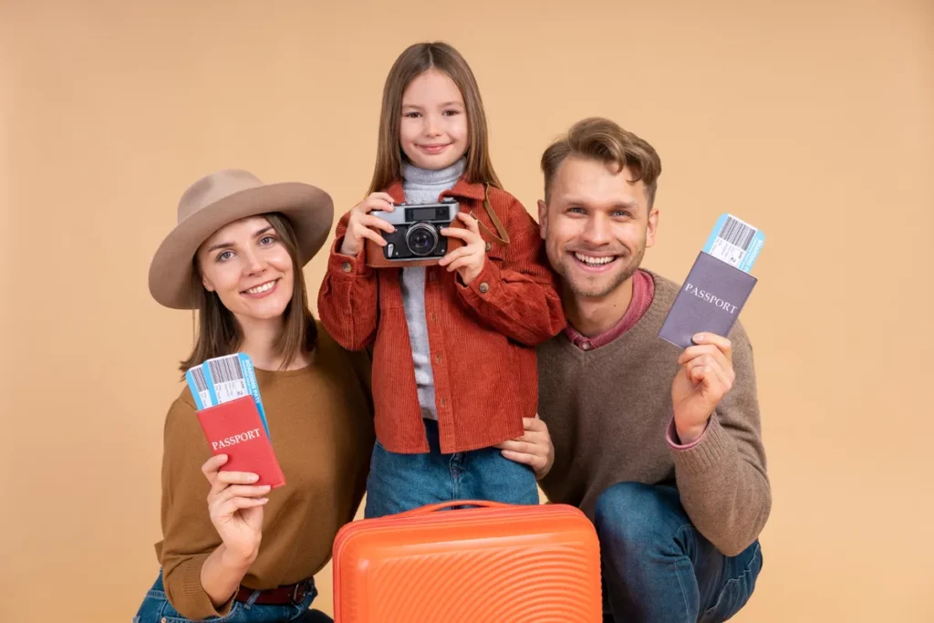 Uma família de três pessoas, um pai, uma mãe e uma filha, sorrindo para a câmera, com a criança segurando uma câmera e os pais segurando passaportes e passagens.