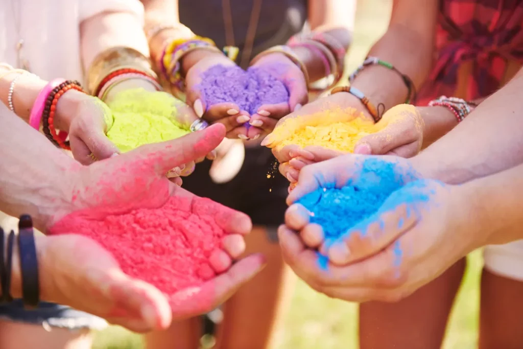 Mãos segurando pós coloridos em vermelho, amarelo, azul, verde e roxo durante a celebração do Holi Festival.