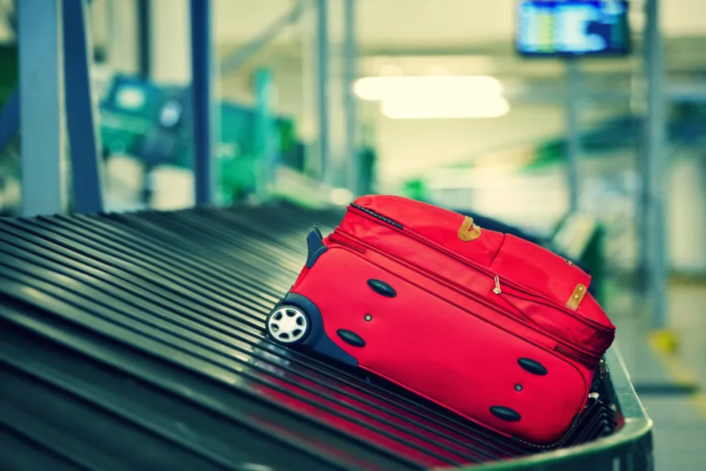 Uma mala de viagem vermelha, sozinha, em uma esteira de bagagem vazia de aeroporto.