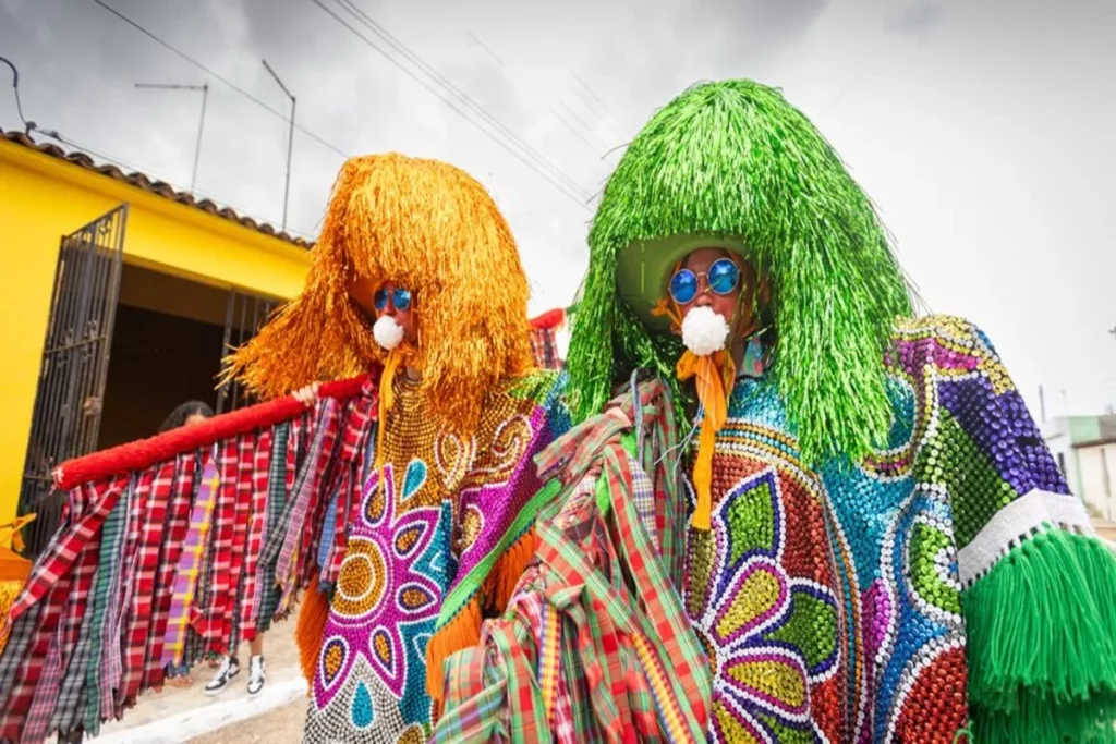 Integrantes do Maracatu com trajes coloridos, chapéus ornamentados e adereços tradicionais durante manifestação cultural no Brasil.
