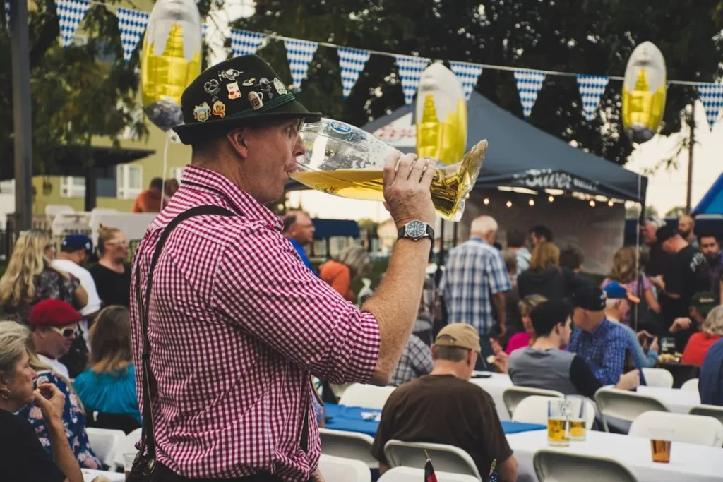 Homem com traje típico alemão bebendo cerveja em grande caneca durante a Oktoberfest ao ar livre.