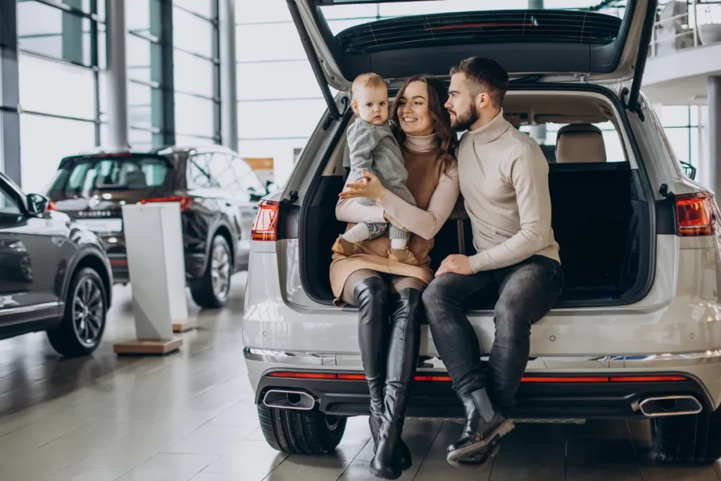 Família com bebê sentada no porta-malas de um carro em uma concessionária, ilustrando a experiência de alugar carro.