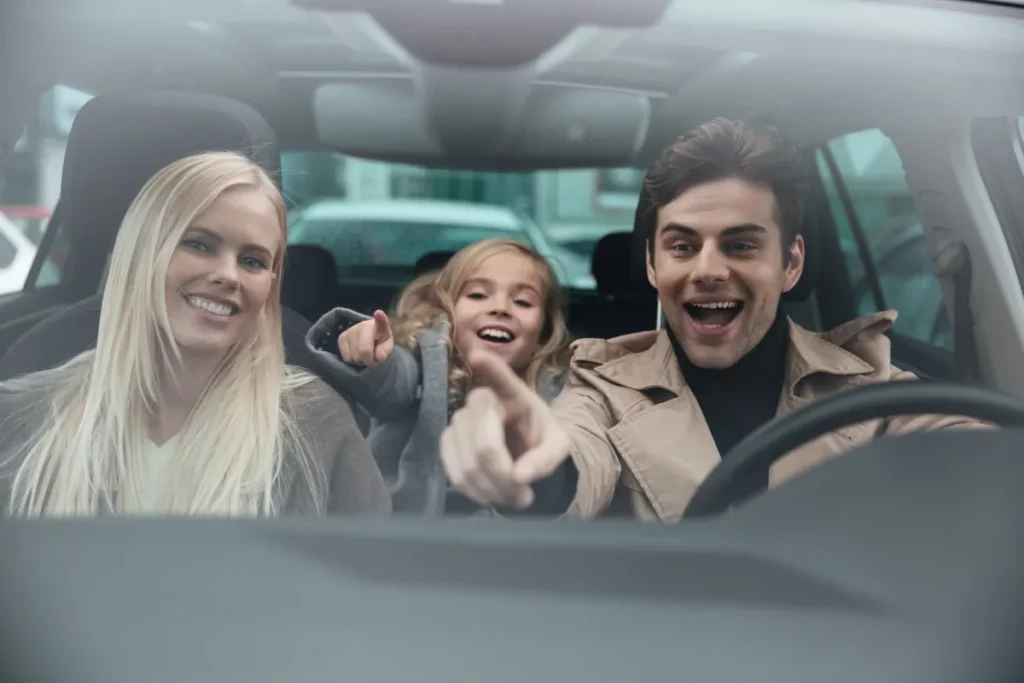 Família feliz no interior de um carro alugado, com a criança apontando para a frente durante a viagem.