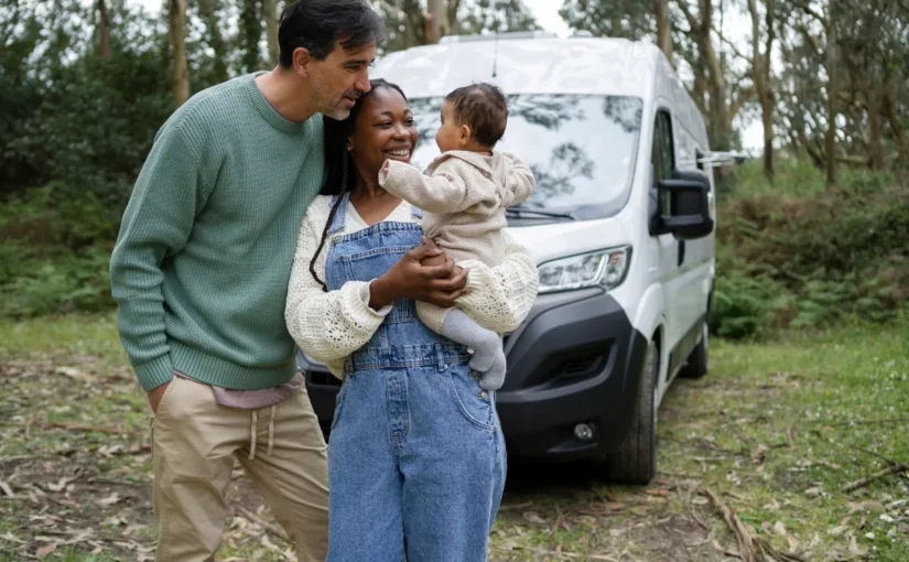 Casal sorridente com bebê nos braços em frente a uma van branca alugada, em meio à natureza.
