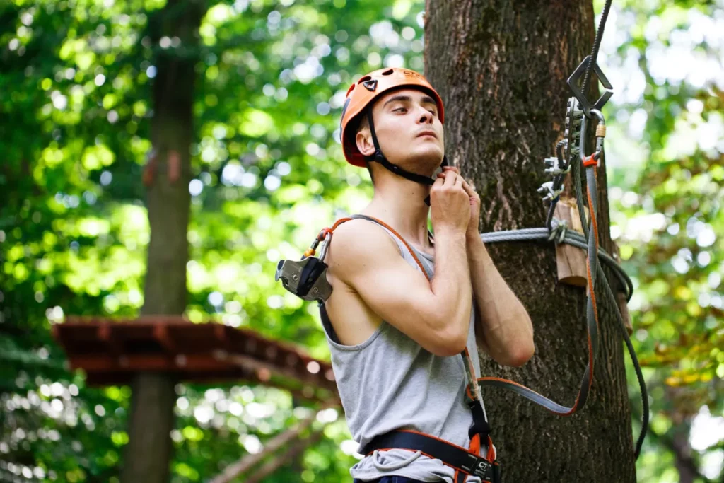 Jovem ajustando capacete e equipamentos de segurança antes de praticar arvorismo em meio à natureza