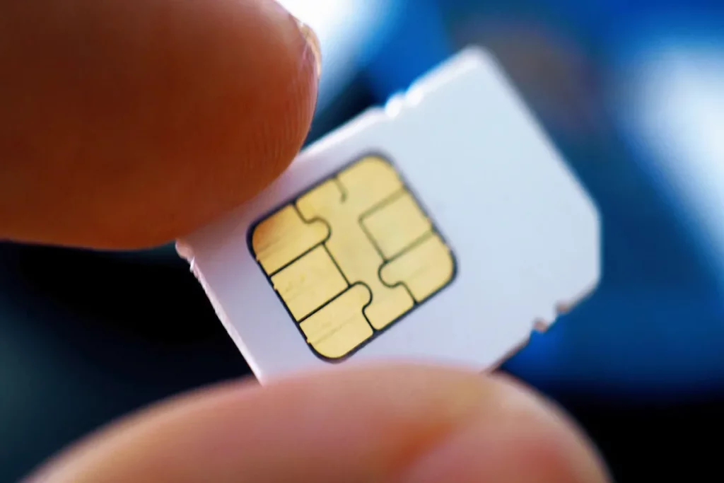 Uma mão segurando um chip de celular, com o foco na parte dourada dos circuitos.