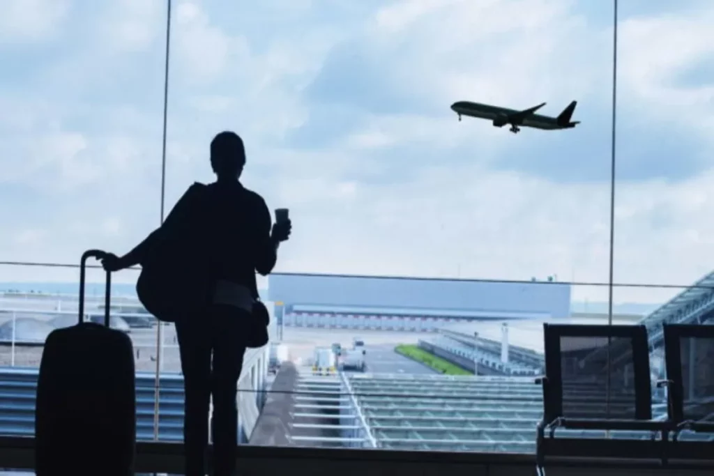 Passageiro no aeroporto com mala observa avião decolando, simbolizando viagens low cost e passagens aéreas econômicas.