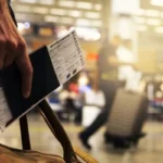 Passageiro segurando passaporte e cartão de embarque no aeroporto, representando viagens low cost e passagens aéreas econômicas.
