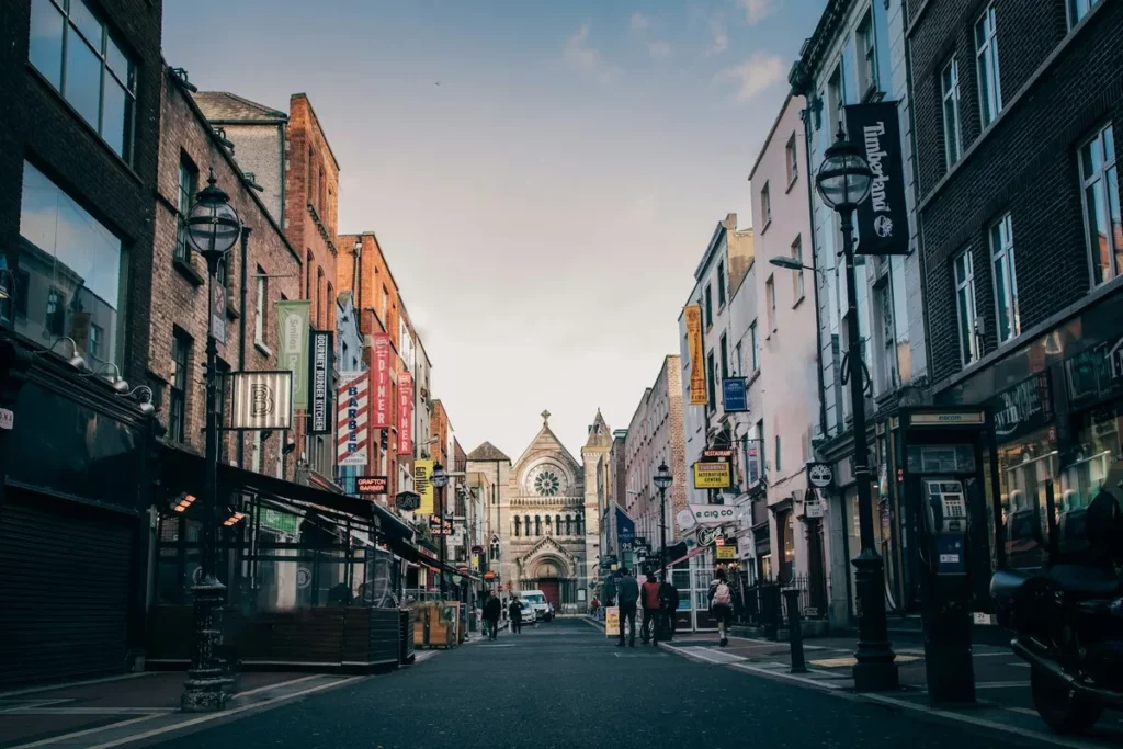 Rua movimentada em Dublin, Irlanda, com lojas, restaurantes e igreja ao fundo, destino ideal para viajar sozinho.