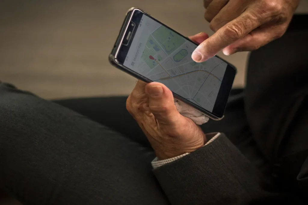 Close-up de um homem mais velho tocando a tela de um smartphone com o polegar para interagir com um aplicativo de mapa, representando a navegação e o uso de mapas offline.