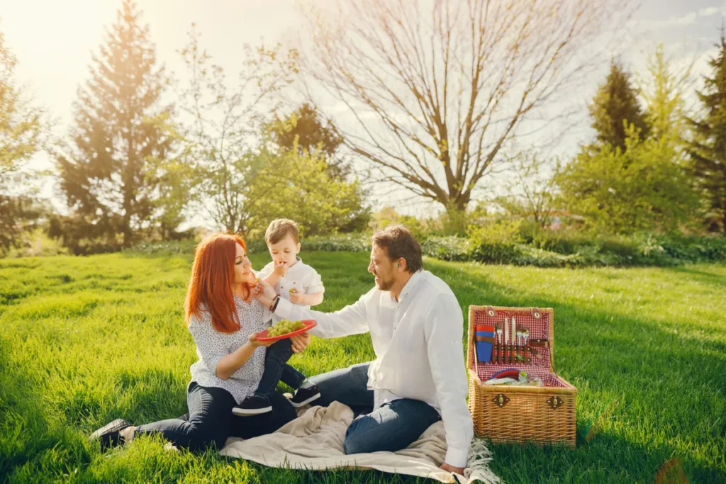 Família com criança desfrutando de piqueniques ao ar livre com frutas e uma cesta.