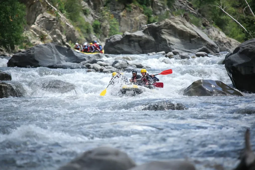 Foto de um bote de rafting com um grupo de pessoas remando em um rio de águas turbulentas.