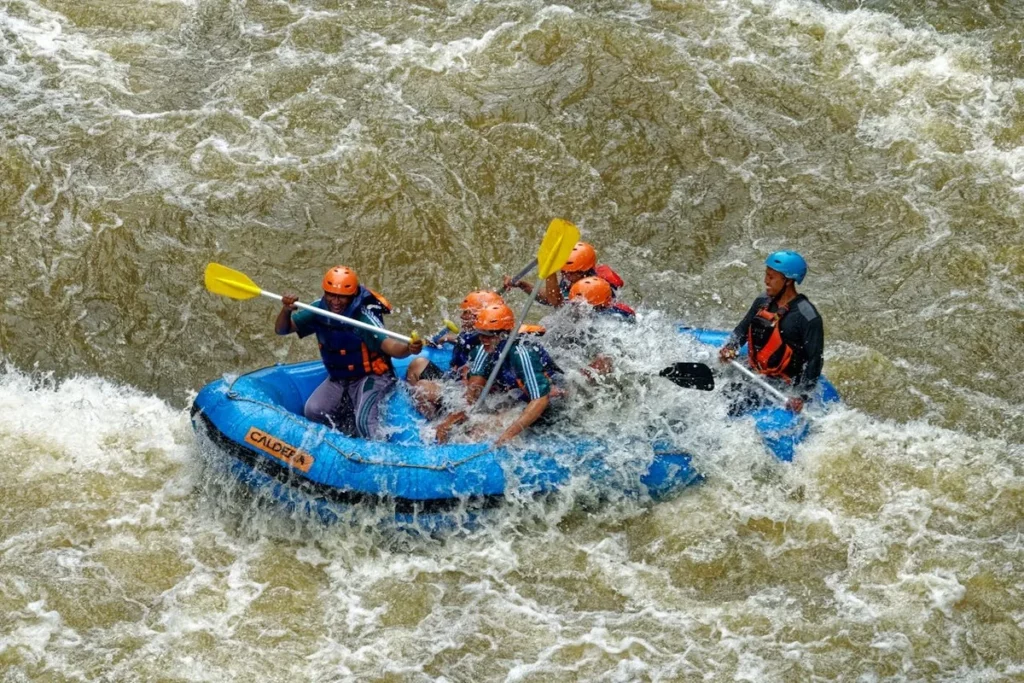 Foto de um bote de rafting com um grupo de pessoas remando em um rio de águas turbulentas.
