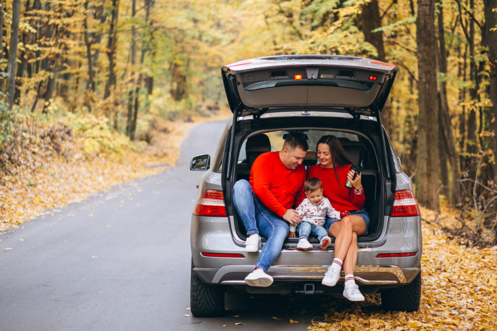 Família com criança pequena sentada no porta-malas do carro em uma road trip de outono.