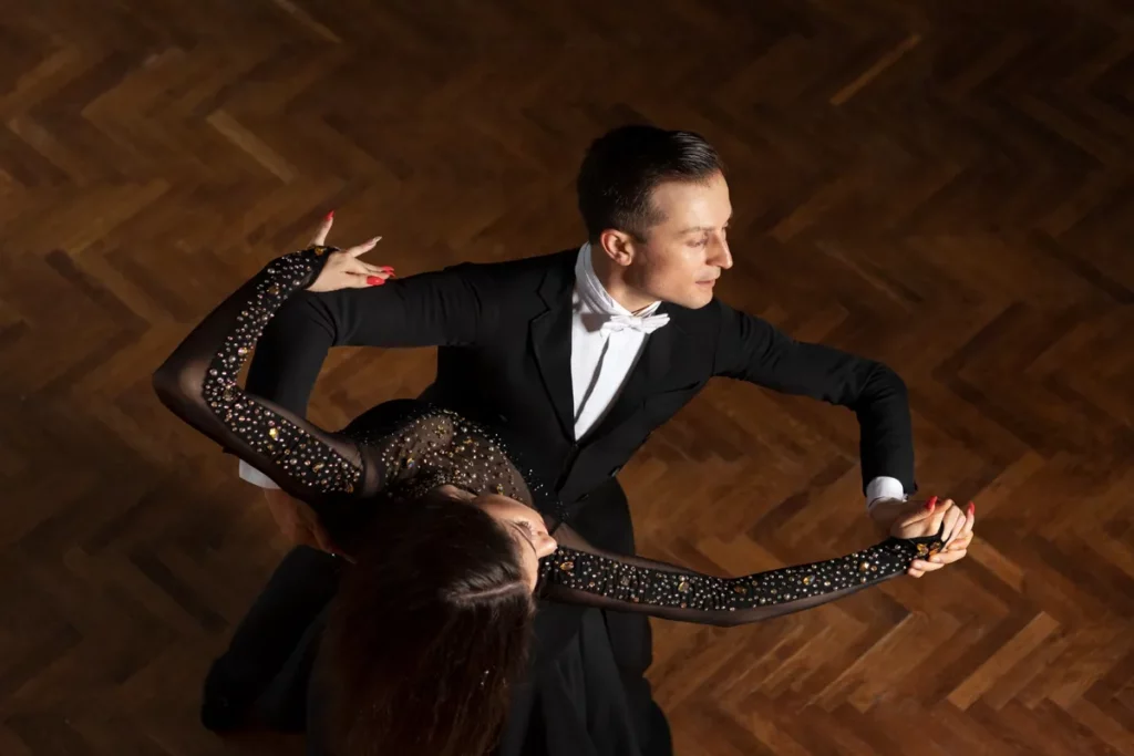 Casal elegantemente vestido dançando tango argentino em salão com piso de madeira.