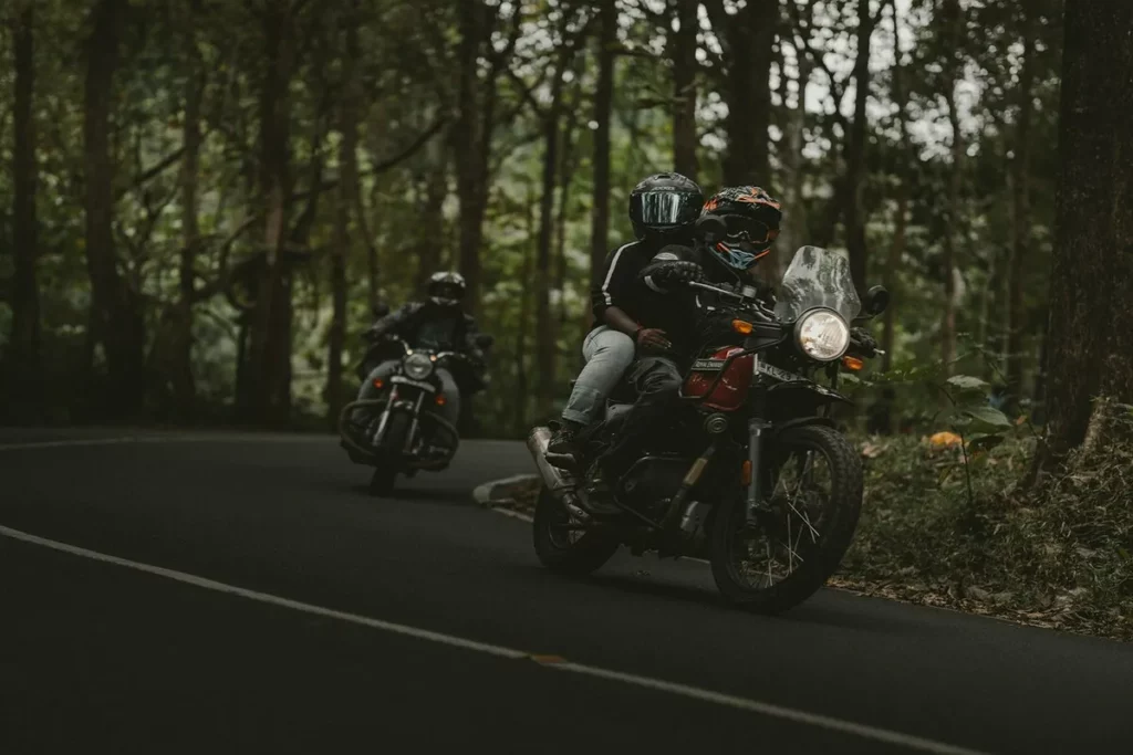 Dois motociclistas usando capacetes pilotando em estrada sinuosa no meio da floresta durante uma viagem de moto.