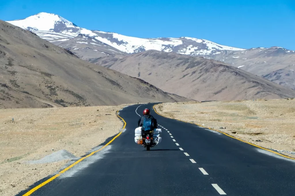 Motociclista viajando sozinho em estrada deserta com montanhas nevadas ao fundo, simbolizando aventura e liberdade.