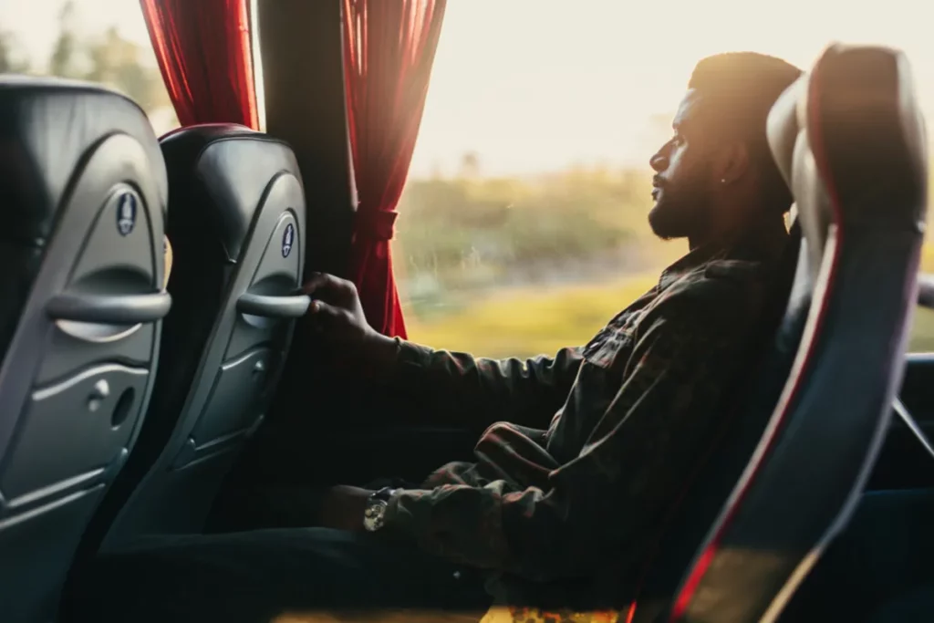 Homem sentado confortavelmente em poltrona de ônibus durante viagem ao pôr do sol.