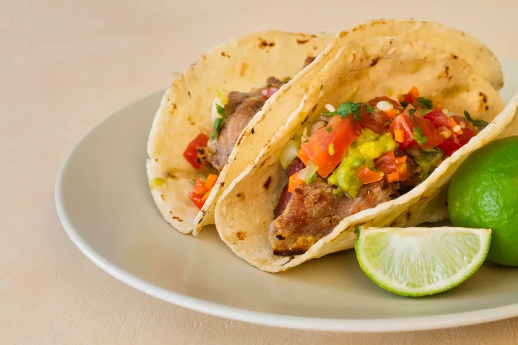Tacos mexicanos com carne grelhada, guacamole e pico de gallo servidos em um prato com fatias de limão