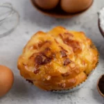 Pastel de Nata caseiro e tostado em close-up, rodeado por ovos, farinha de trigo e batedor de arame, ingredientes de doçaria portuguesa.