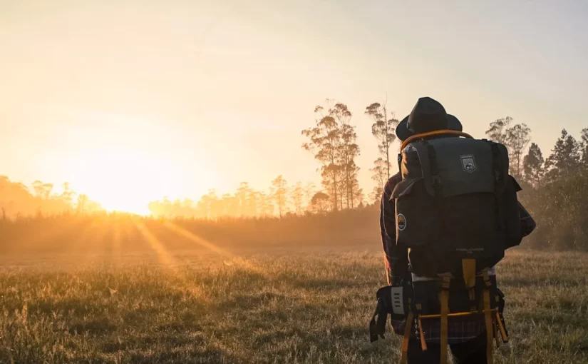 Homem com mochila nas costas, vendo o pôr do sol