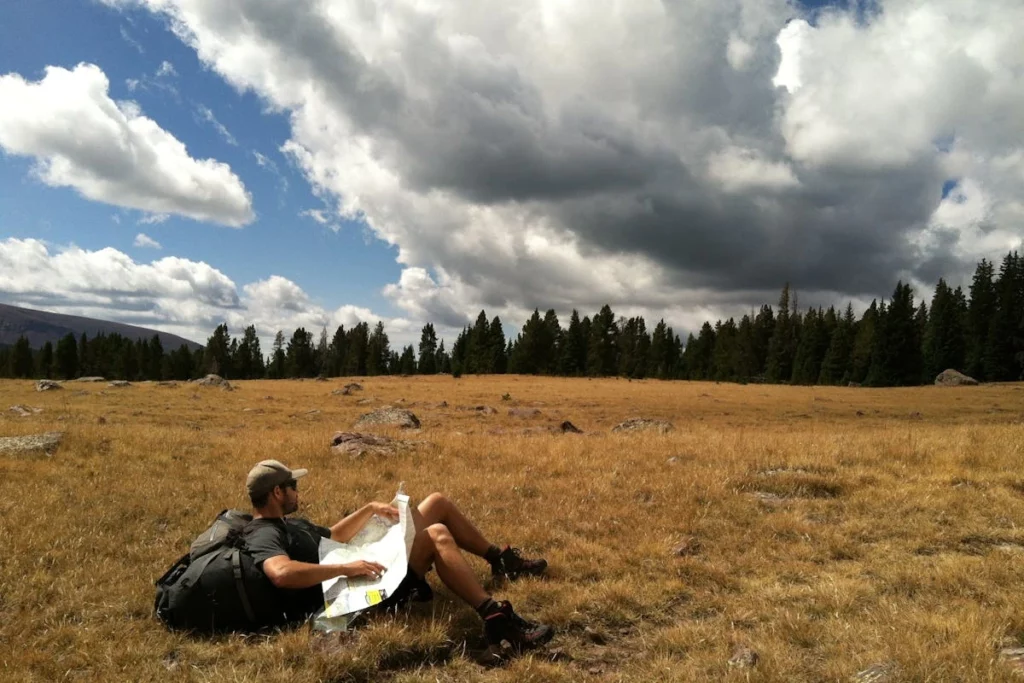Pessoa sentada, apoiada em uma mochila, no meio de um campo 