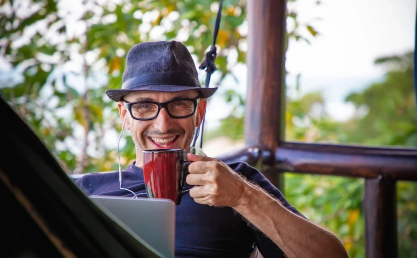Homem em uma rede, tomando café e com seu laptop