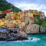 Cinque Terre: como visitar as vilas coloridas à beira-mar da Itália? Casas coloridas construídas na encosta rochosa de Manarola com o mar azul na costa de Cinque Terre, Itália.